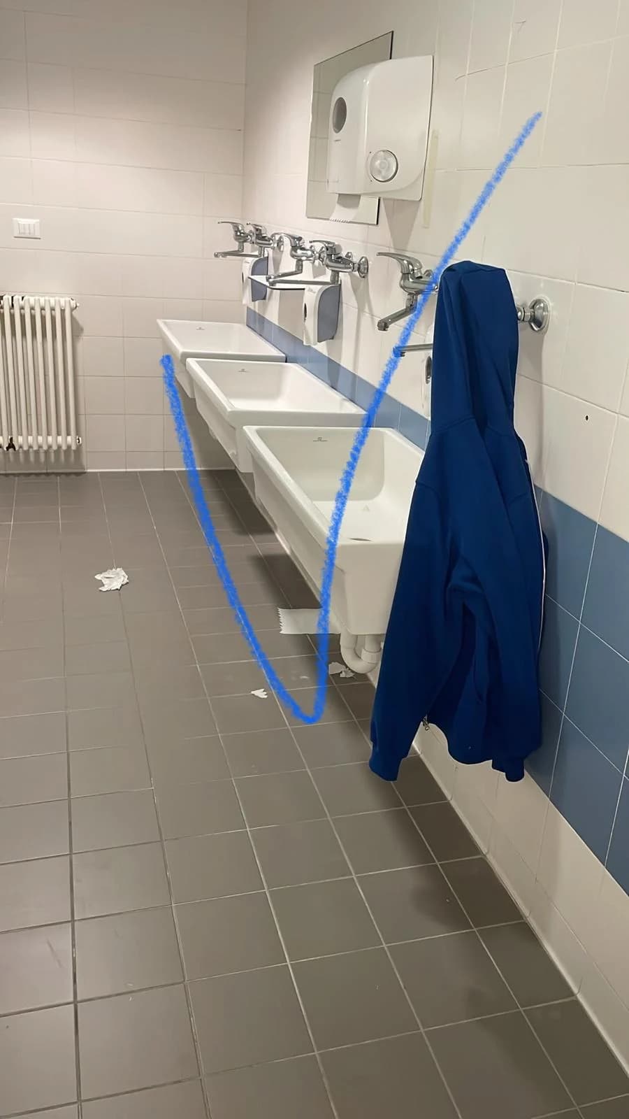 Fila di lavabi con rubinetti a parete in un bagno condiviso.