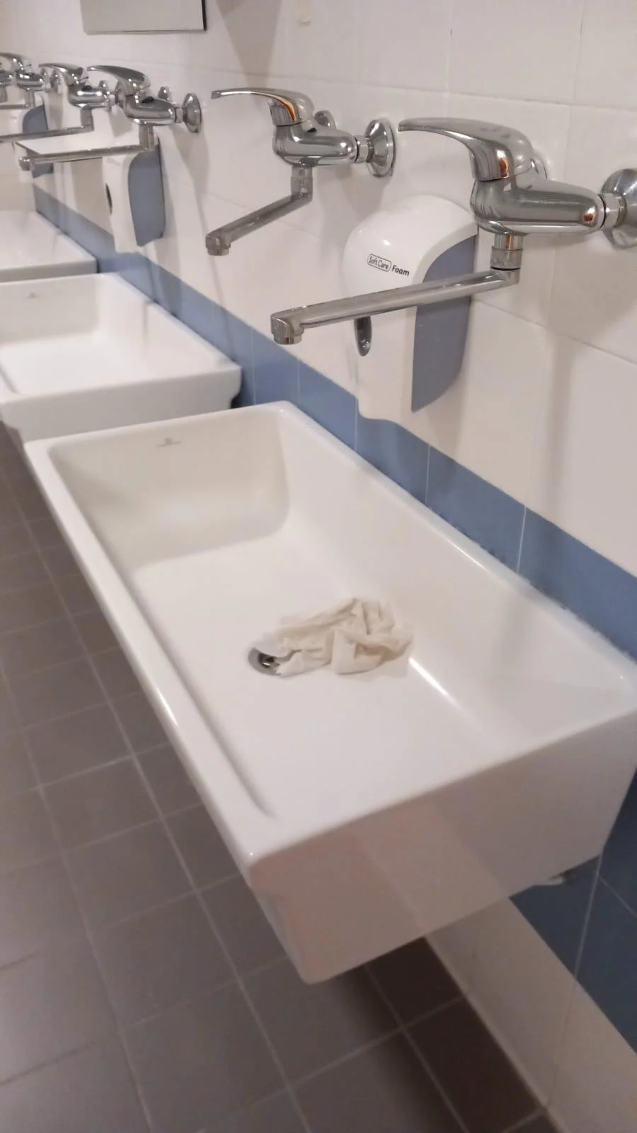 Rubinetti a parete sopra una fila di lavabi bianchi.