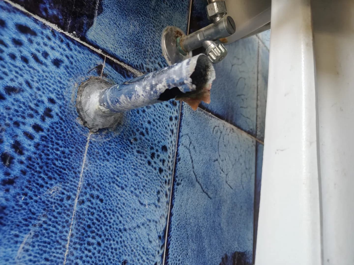 Vecchio raccordo metallico dello scarico del lavabo, corroso e perforato.