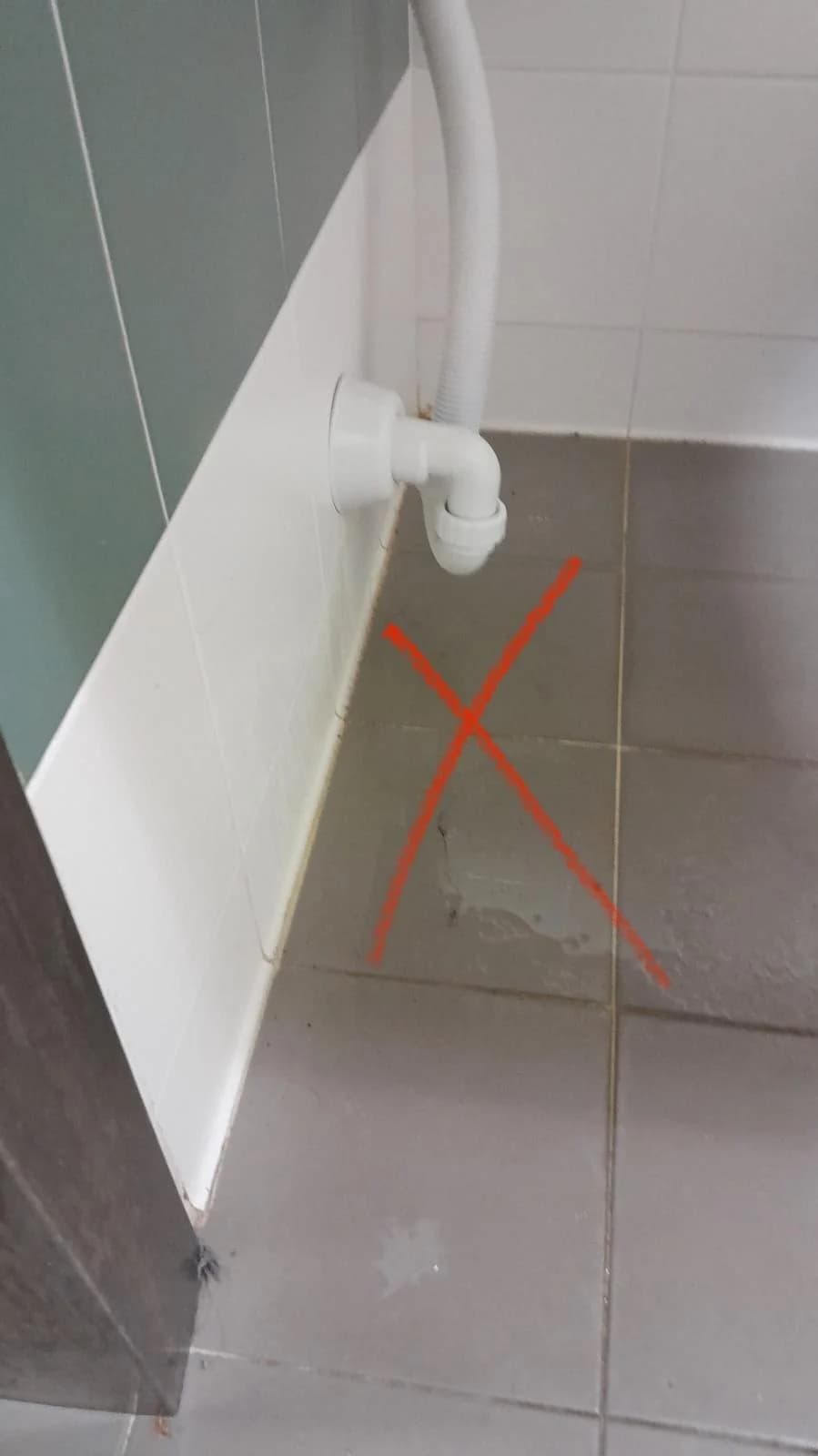 Scarico flessibile collegato a un sifone a parete sopra un pavimento bagnato.